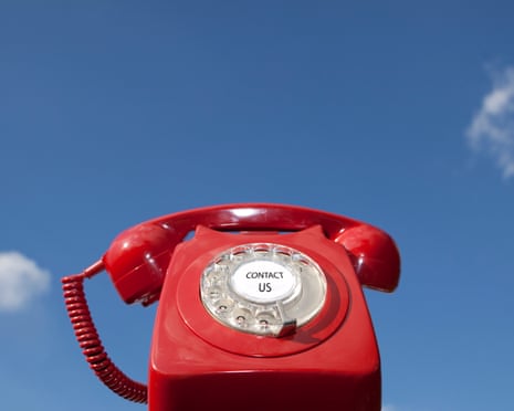 Red old-fashioned telephone with the words 'contact us' in the centre of the dialling pad, against a blue sky