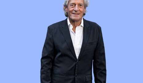 Actor Nigel Havers in black jacket and white shirt against purple background