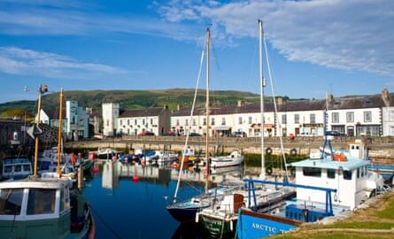 Colourful fishing boats sit in a harbour in front of a line of white terraced cottages