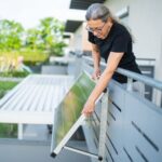 A woman adjusts a solar panel on the balcony of a house