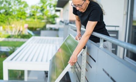A woman adjusts a solar panel on the balcony of a house