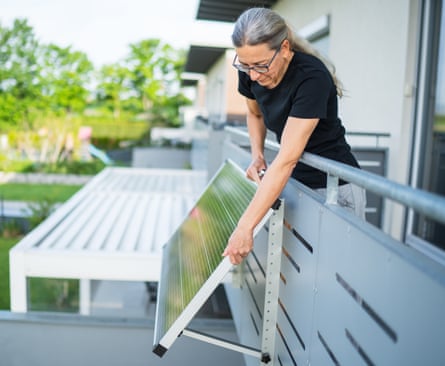 A woman adjusts a solar panel on the balcony of a house