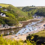 A sea inlet at the bottom of a green steep-sided valley with sand and water at the bottom and boats moored.