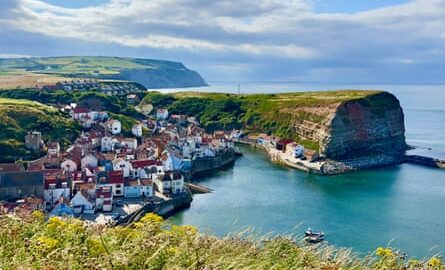 An elevated view of a traditional historic fishing village, with colourful cottages tumbling down the hillside to the sea and harbour.