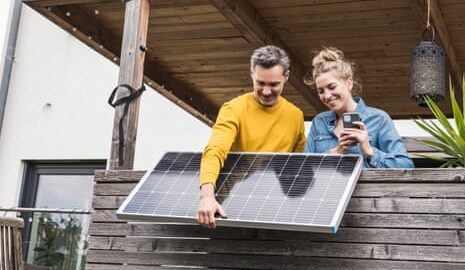 A couple install a solar panel on a wooden balcony