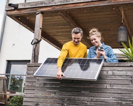 A couple install a solar panel on a wooden balcony