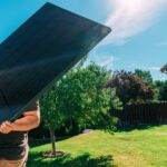 A man lifts a large solar panel in the garden of a US home