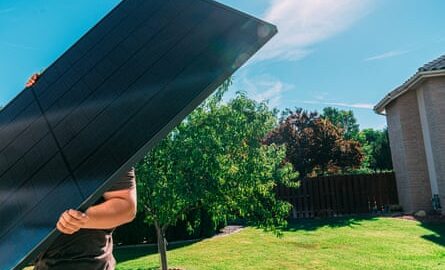 A man lifts a large solar panel in the garden of a US home