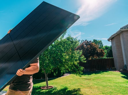 A man lifts a large solar panel in the garden of a US home