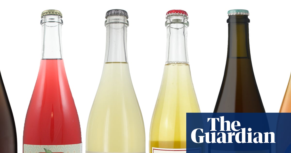 Six Pet Nat wine bottles with colourful labels and varying liquid colours stand in a row