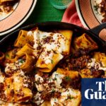 Turkish lamb and hot pepper paccheri in a pan with a wooden spoon, and served on three plates next to the pan, all placed on a green cloth with napkins and glasses of water.
