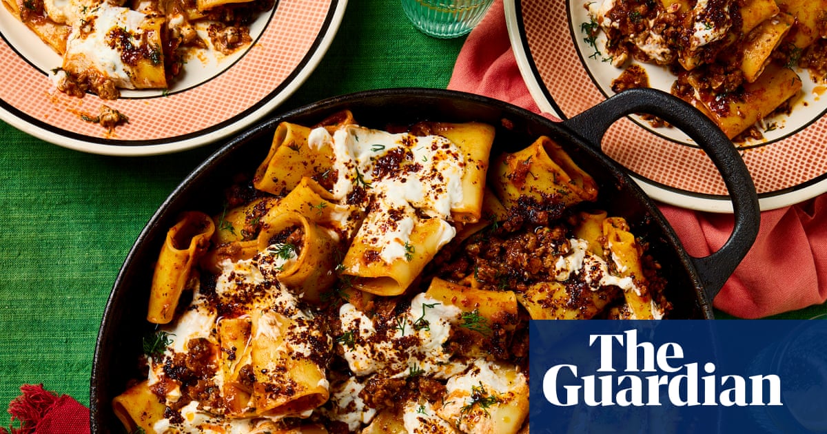 Turkish lamb and hot pepper paccheri in a pan with a wooden spoon, and served on three plates next to the pan, all placed on a green cloth with napkins and glasses of water.