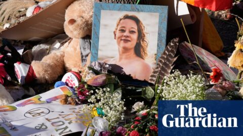 A memorial for Renee Good with flowers, a teddy bear, signs, and her framed photo