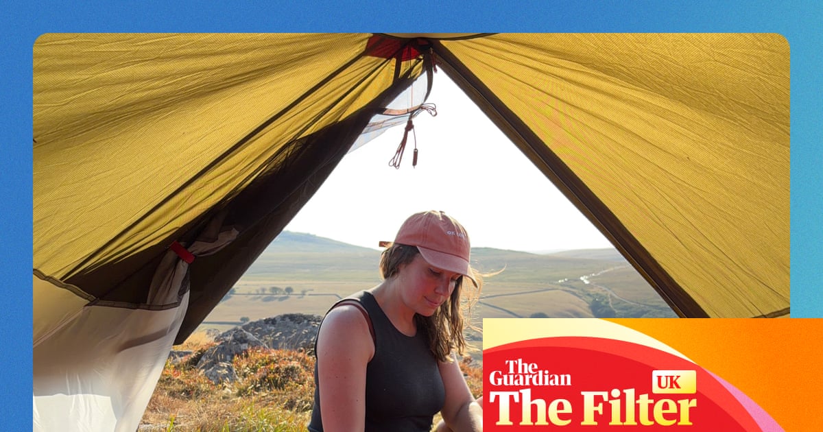 Sian Lewis sits at a tent entrance using a camping stove, with hills in the background